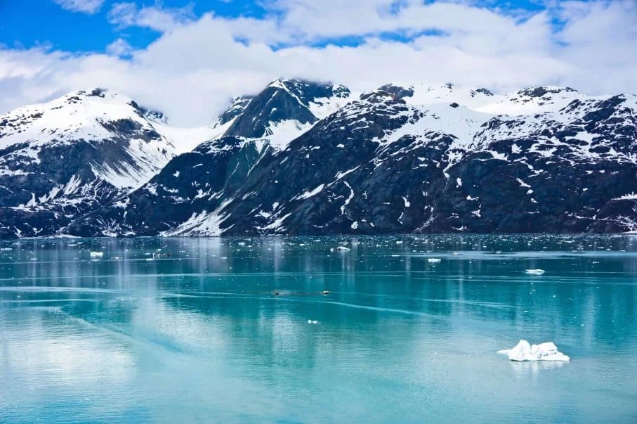 Snow-covered mountains reflected in a turquoise glacial lake under a partly cloudy sky. Snow-covered mountains reflected in a turquoise glacial lake under a partly cloudy sky.
